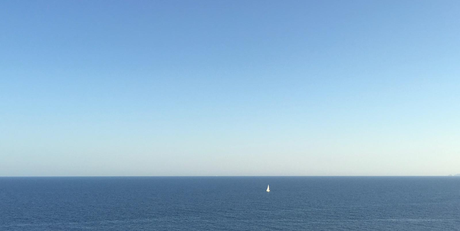 Kleines Segelboot auf offenem Meer unter weitem Himmel